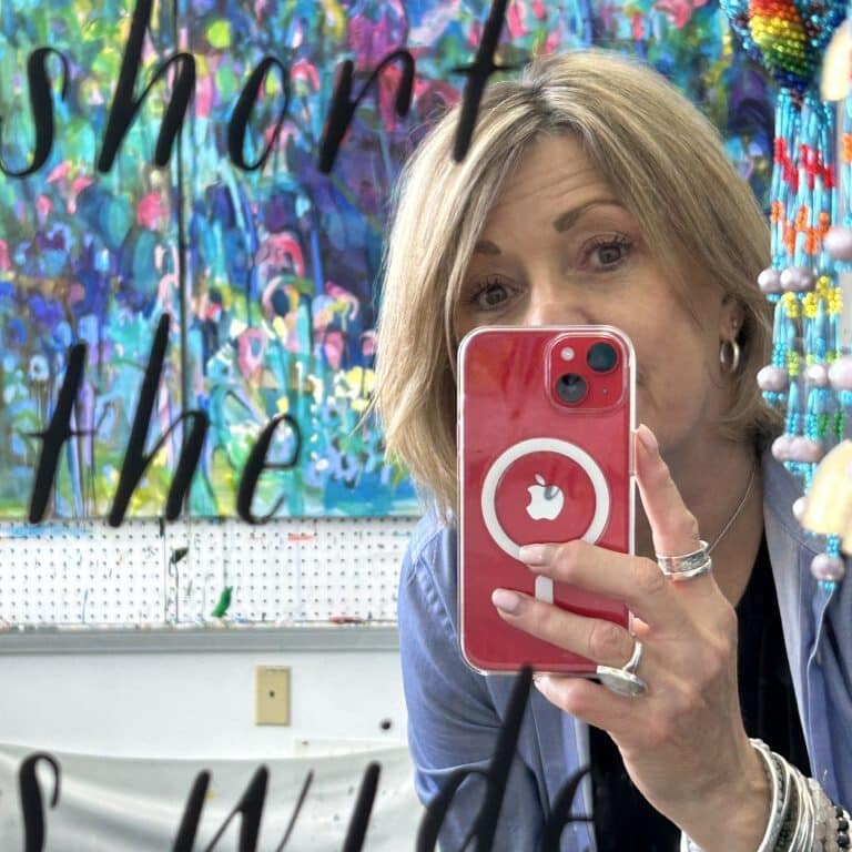 Woman holding phone in front of mirror and colourful painting