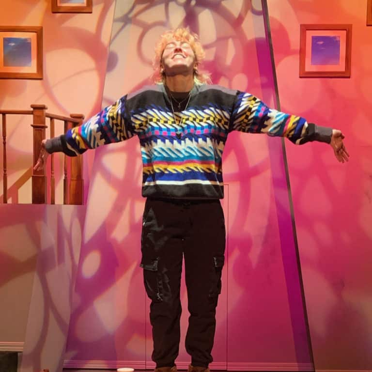 Anika standing on pink lit stage with arms out