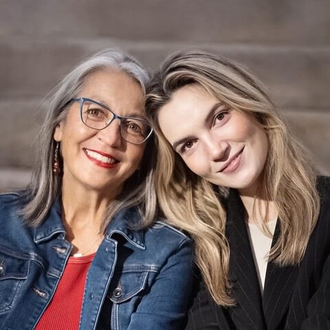 Two women with heads against each other facing the camera smiling